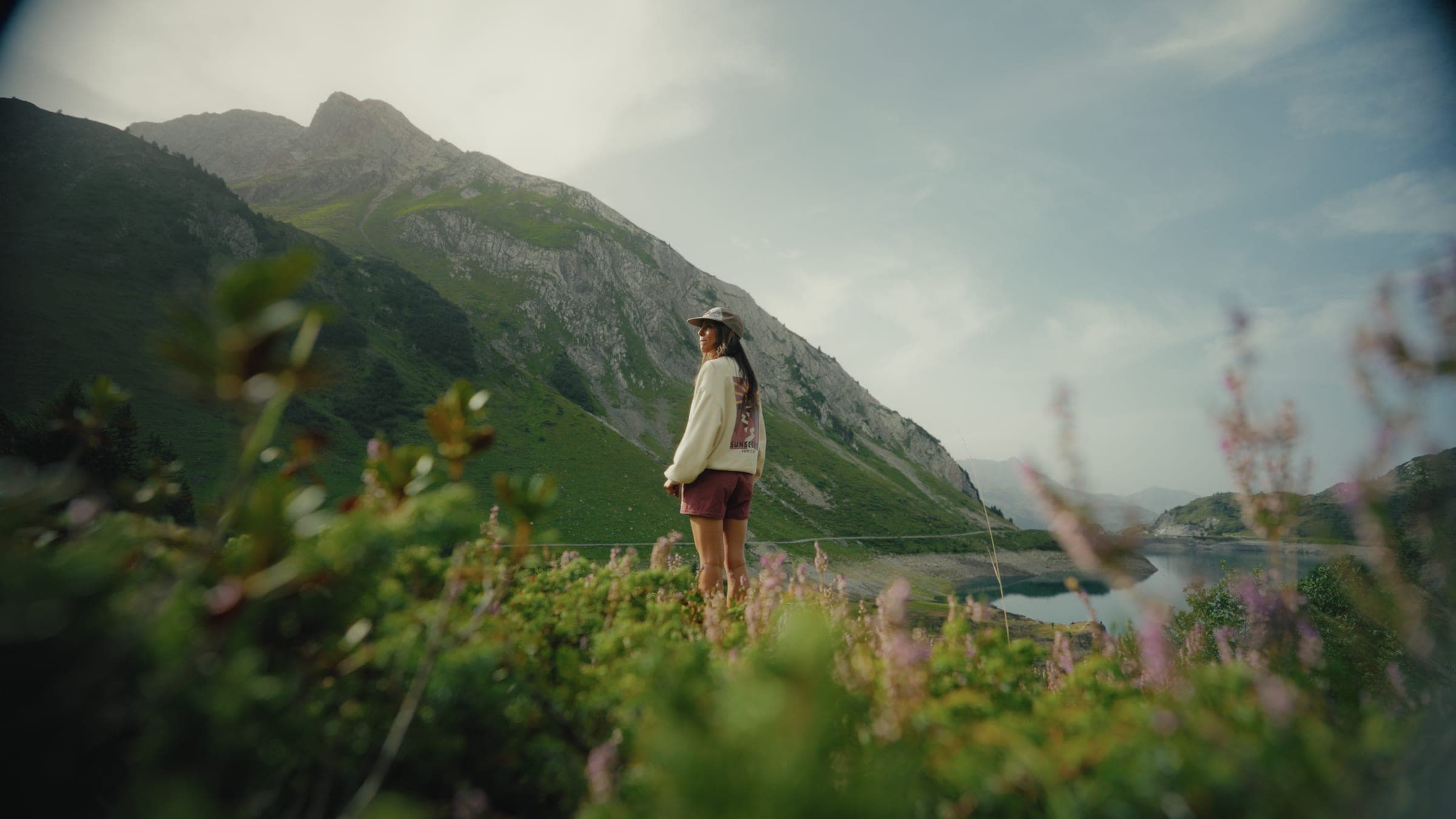 The same alpine lake frame after grading, with soft pastel flowers and a cool valley